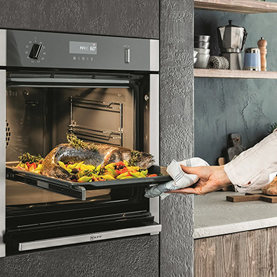 Person taking food out of a built-in oven in a modern kitchen. Links to Built-In Oven Category Page